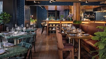 A restaurant interior with wooden tables, green chairs, and a bar area.