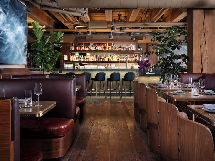 Interior de un restaurante con cabinas de madera, zona de bar y una variedad de botellas en estanterías.