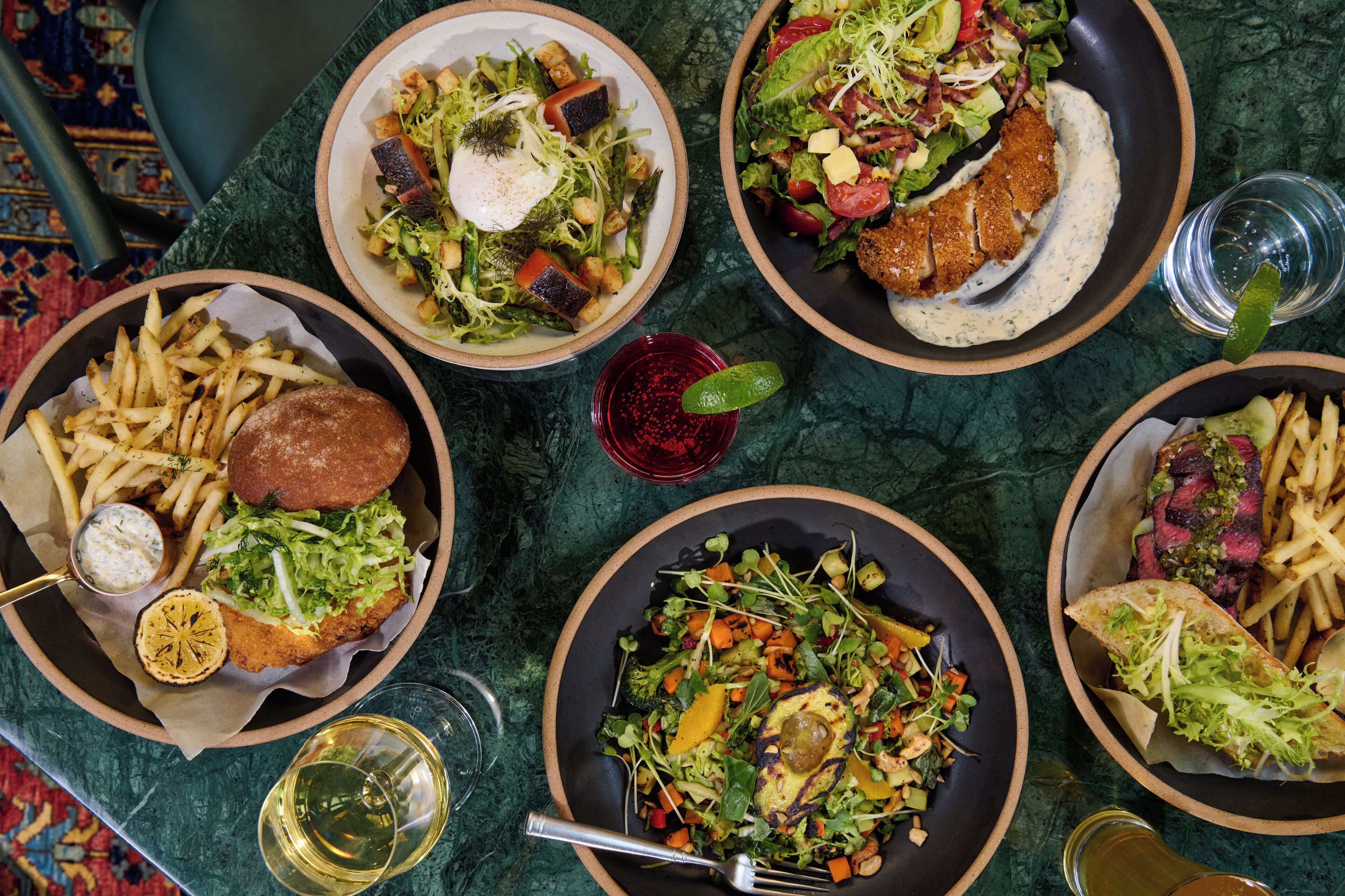 A table with various dishes including salads, fries, and a burger.