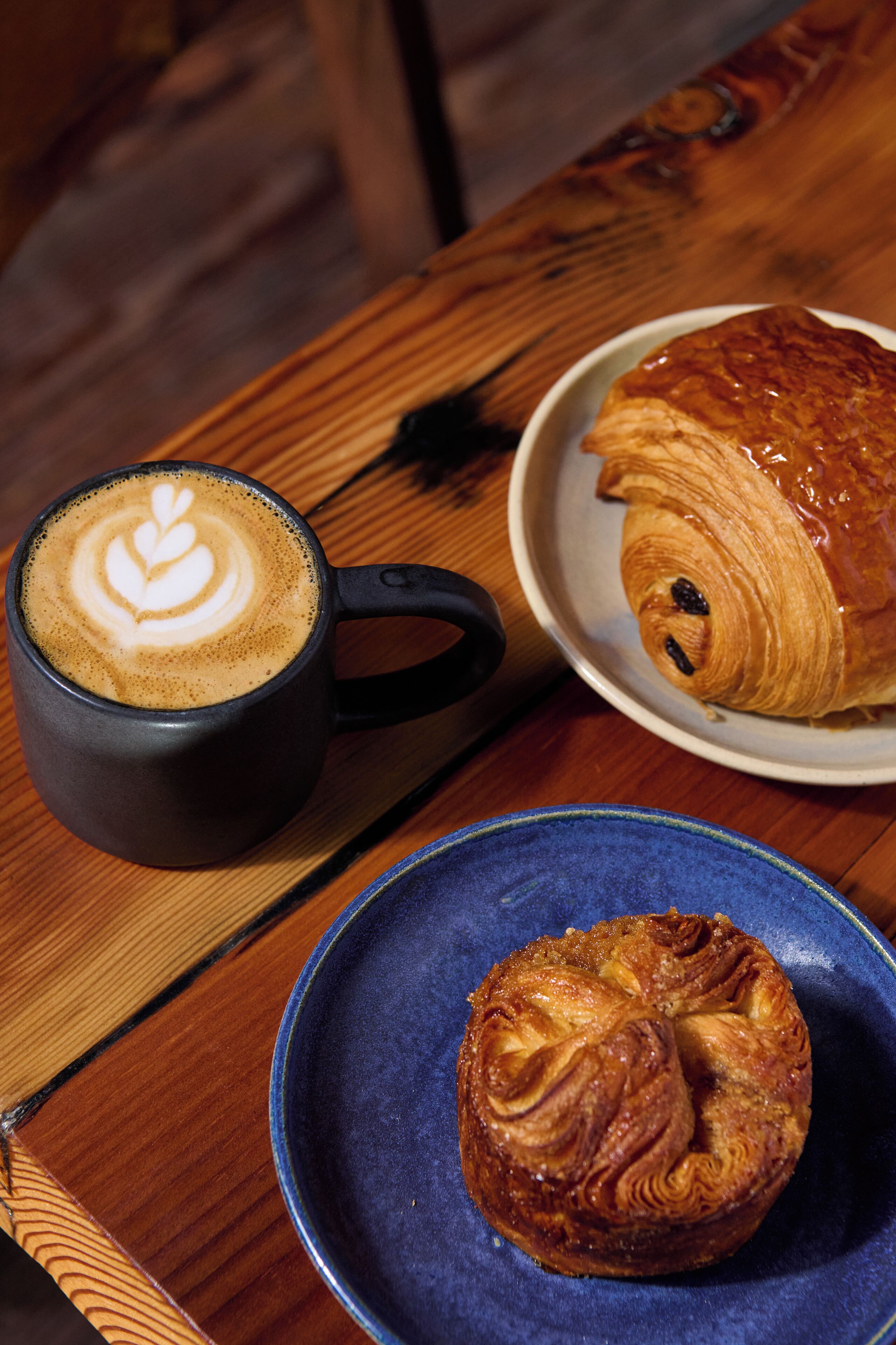 A table with a coffee cup, a croissant, and a pastry on a blue plate.