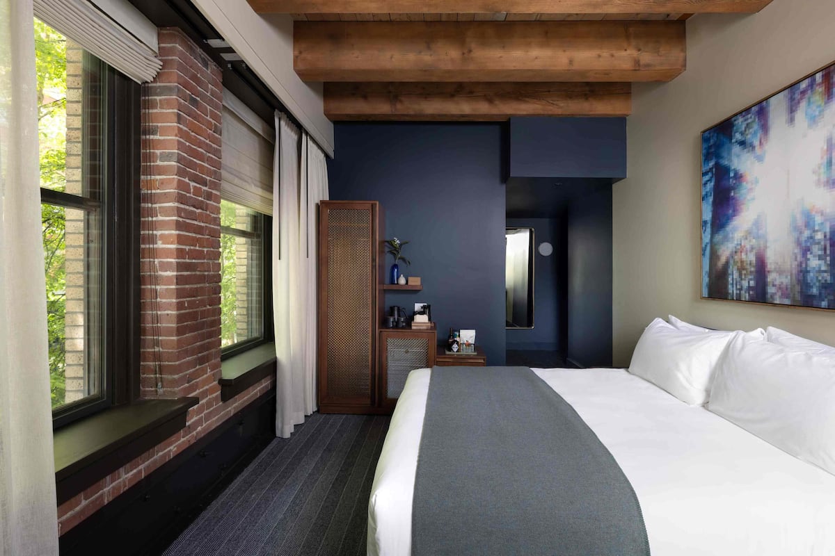 A hotel room with a large bed, a brick fireplace, a wooden cabinet, and a painting on the wall.