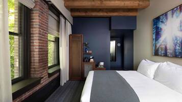 A hotel room with a large bed, a brick fireplace, a wooden cabinet, and a painting on the wall.