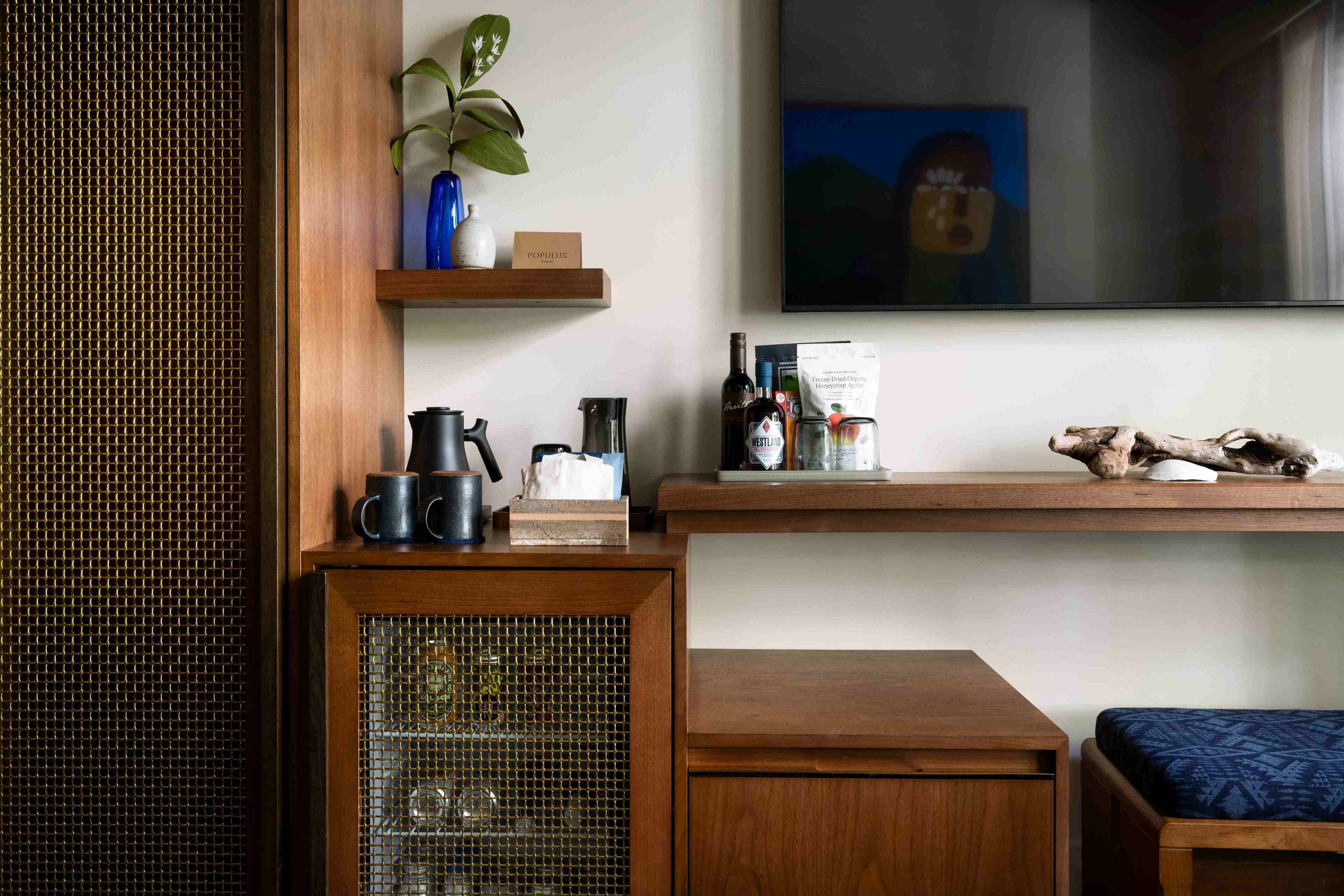 Una habitación con un armario de madera, una pequeña mesa, un banco acolchado azul, una estantería con adornos y un cuadro en la pared.