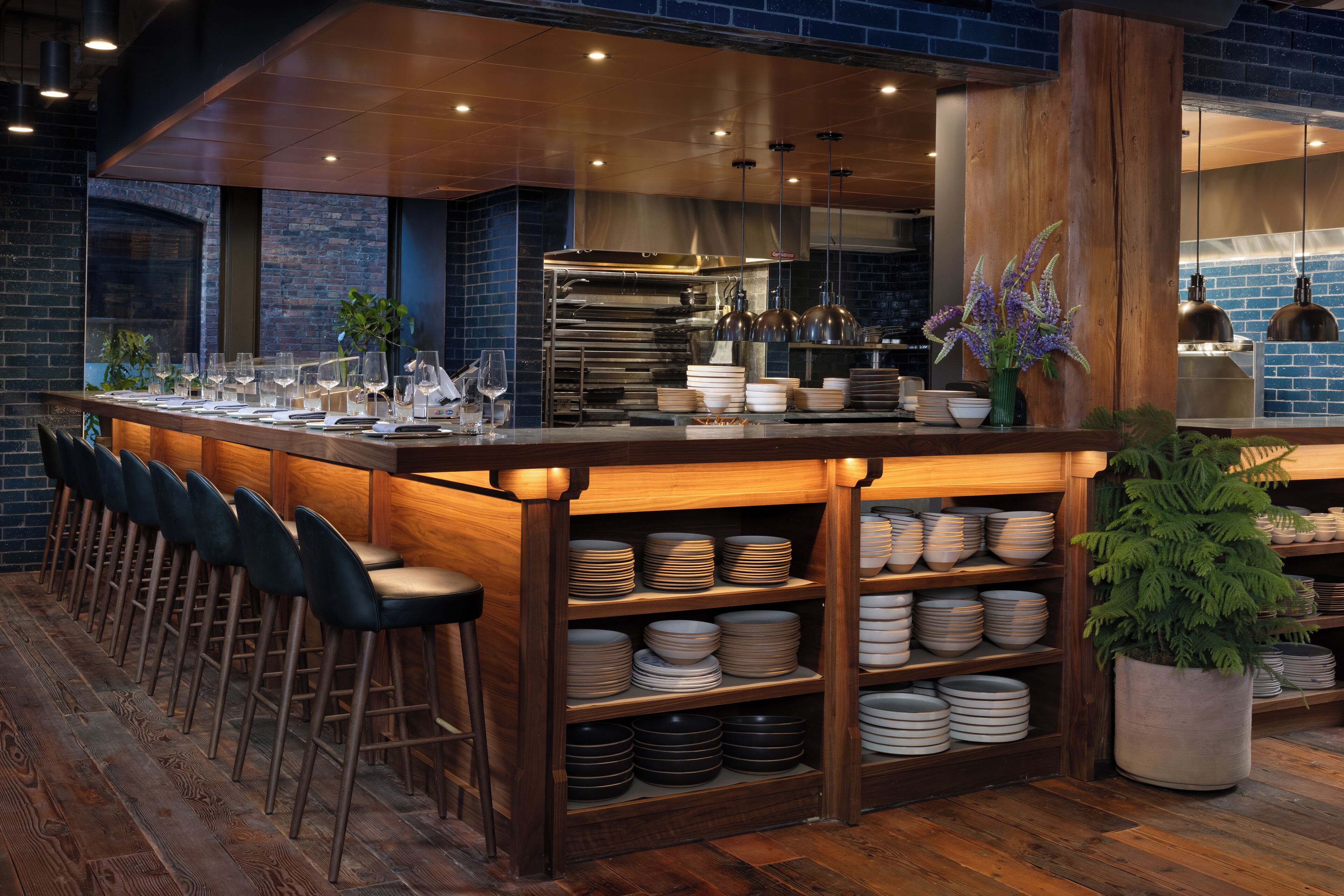 A bar area with a long counter, multiple stools, and shelves stocked with plates and glasses.