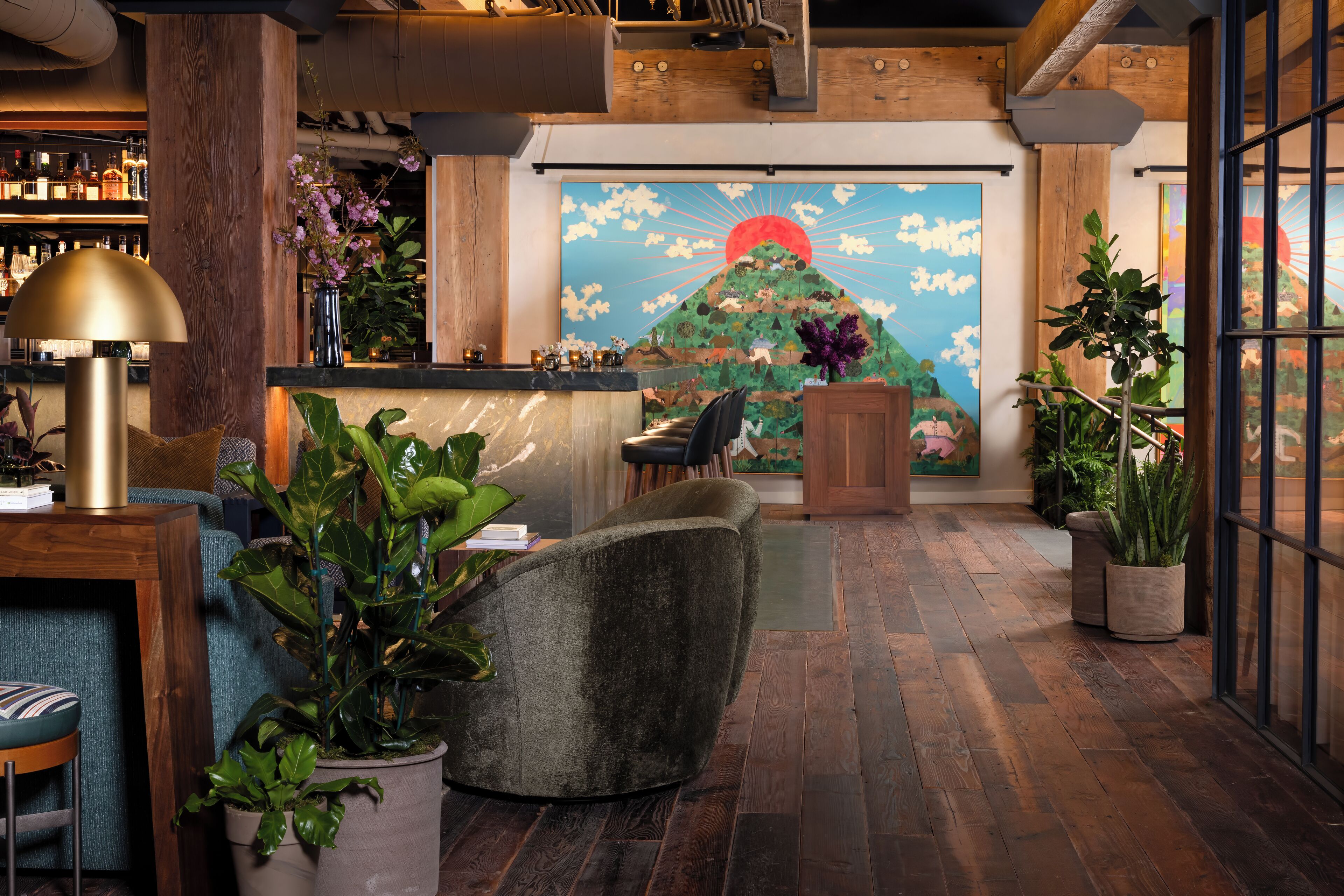 A lobby with a wooden floor, a reception desk, a large painting of a mountain, and various plants.