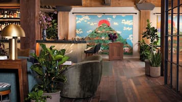 A lobby with a wooden floor, a reception desk, a large painting of a mountain, and various plants.