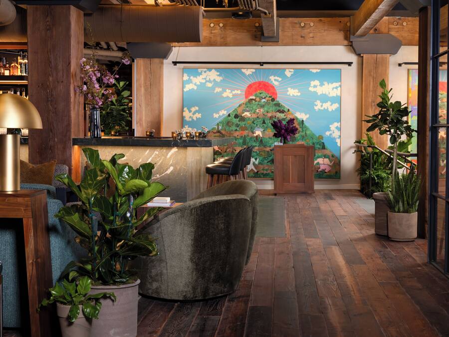 A lobby with a wooden floor, a reception desk, a large painting of a mountain, and various plants.