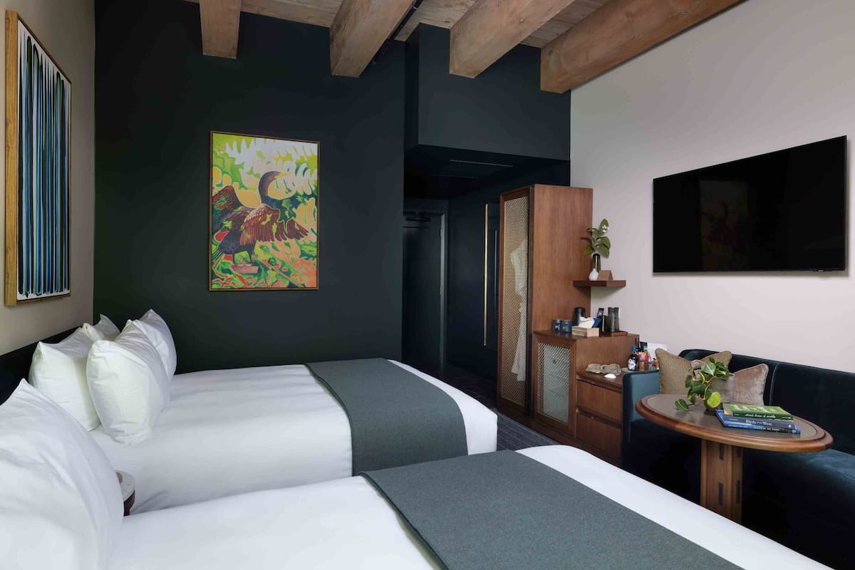 A hotel room with two beds, a small table with books, a TV, and a painting on the wall.