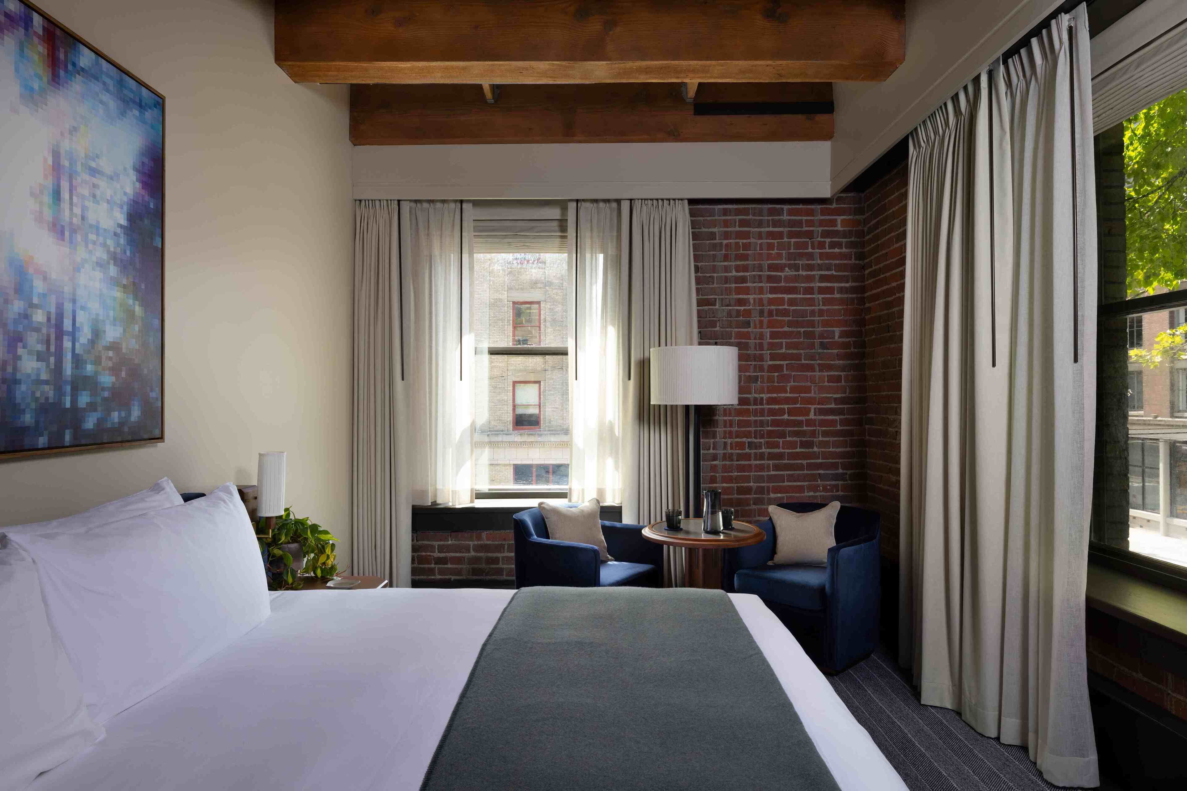 Una habitación de hotel con una cama grande, dos sillones, una mesita y un ventanal con cortinas.