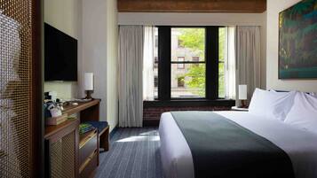 Habitación de hotel con una cama grande, un escritorio con televisor de pantalla plana, una ventana con cortinas y un cuadro en la pared.