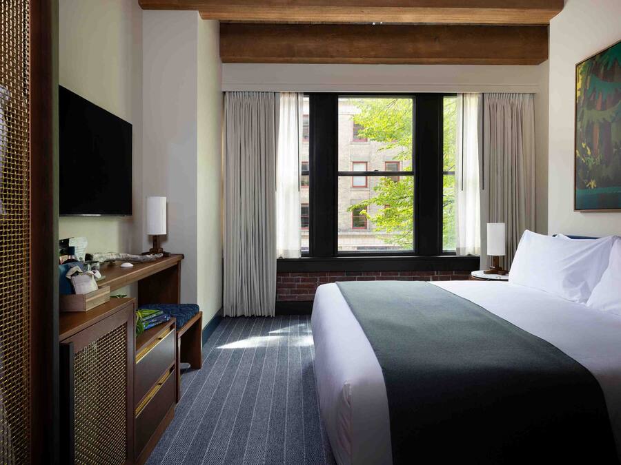 Habitación de hotel con una cama grande, un escritorio con televisor de pantalla plana, una ventana con cortinas y un cuadro en la pared.