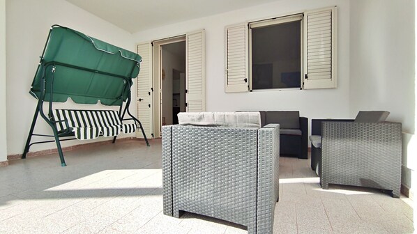 A room with a green outdoor seating area, a sofa, two armchairs, and a small table.
