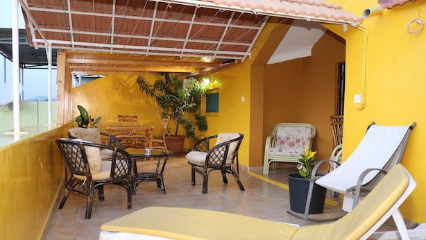 Un balcón con sillas de mimbre, un sillón de descanso y plantas en macetas.