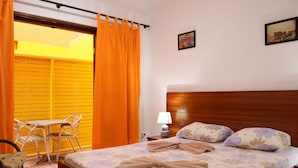 Habitación de hotel con cama, una mesita, sillas, una lámpara y vista a un edificio amarillo por la ventana.