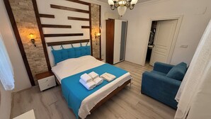 A bedroom with a bed, a blue sofa, a wooden headboard, and a chandelier. - Assos Mia Konaklama ve Restaurant (Ayvacik)