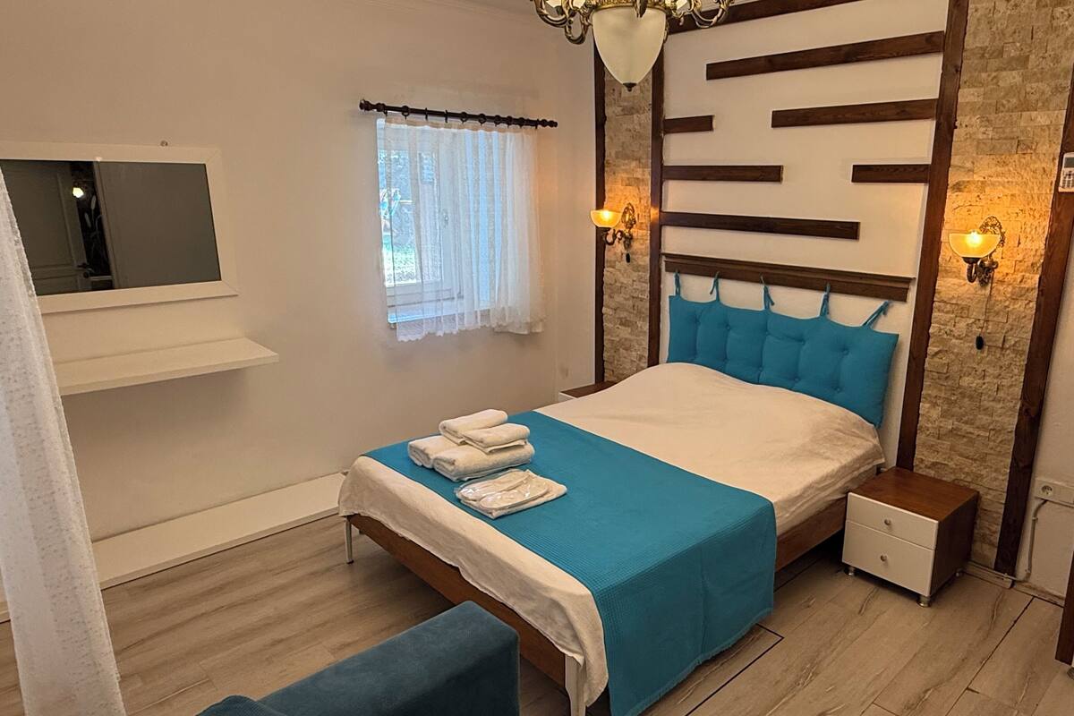 A bedroom with a bed, bedside tables, a TV, a window with curtains, and a stone wall.