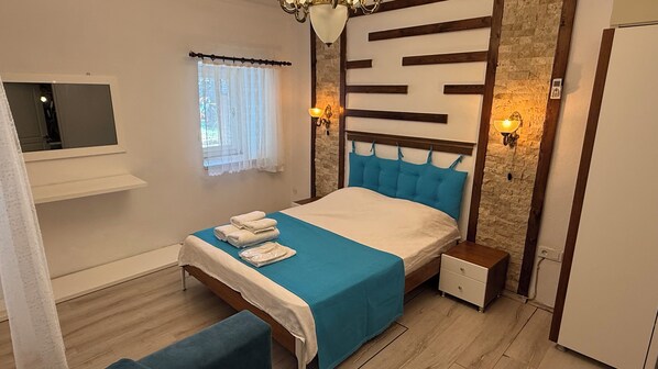 A bedroom with a bed, bedside tables, a TV, a window with curtains, and a stone wall.