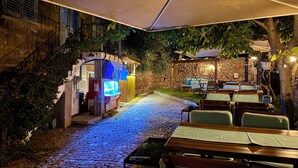 A stone-paved outdoor area with wooden tables and chairs, a small kiosk, and a stone wall. - Assos Mia Konaklama ve Restaurant (Ayvacik)