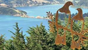 A scenic view of a lake with mountains in the background and a metal sculpture of birds on a branch in the foreground. - Kūkupa Matairangi at Akaroa Lavender (Duvauchelle)