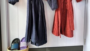 Two bathrobes hanging on a door, a woven basket with slippers, and a tiled floor. - Kūkupa Matairangi at Akaroa Lavender (Duvauchelle)