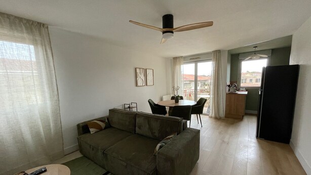 A living room with a sofa, a dining table, and a kitchen area.