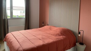 A bedroom with a bed, a ceiling fan, a window with curtains, and a wall with vertical blinds.