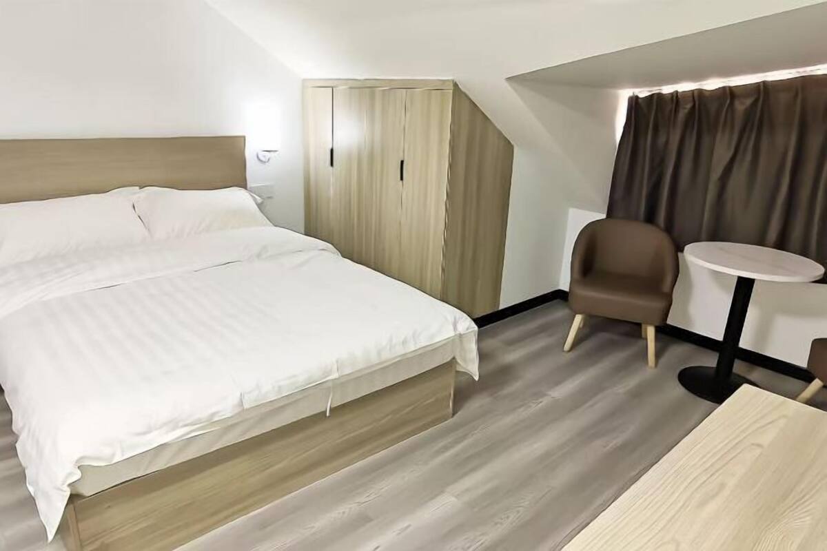 Ein modernes Hotelzimmer mit einem Bett, einem kleinen runden Tisch, einem Sessel und einem Kleiderschrank.