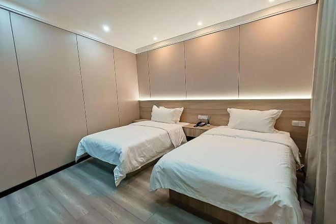 Habitación de hotel con dos camas, cabecero de madera, mesita de noche con teléfono y suelo de color claro.