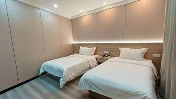 Habitación de hotel con dos camas, cabecero de madera, mesita de noche con teléfono y suelo de color claro.