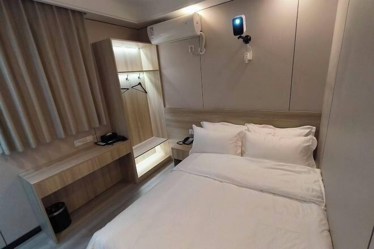 Ein Hotelzimmer mit Bett, Nachttisch, Lampe, Kleiderschrank und Klimaanlage.