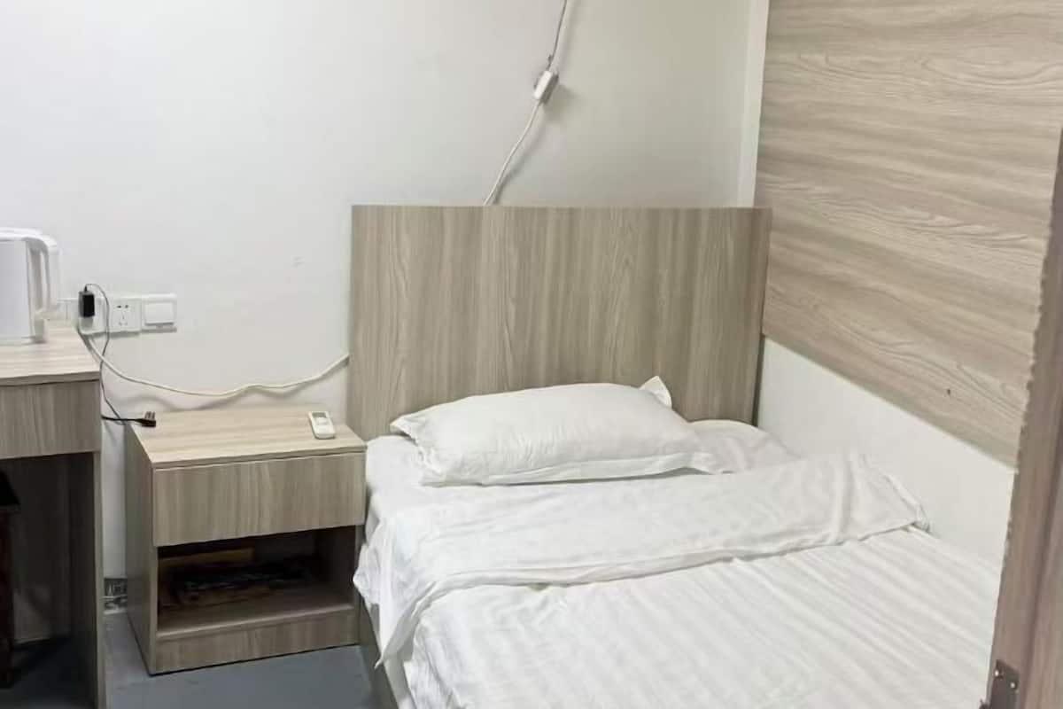 Ein Einzelbett mit weißer Bettwäsche, ein Nachttisch mit Telefon und eine Steckdose an der Wand.