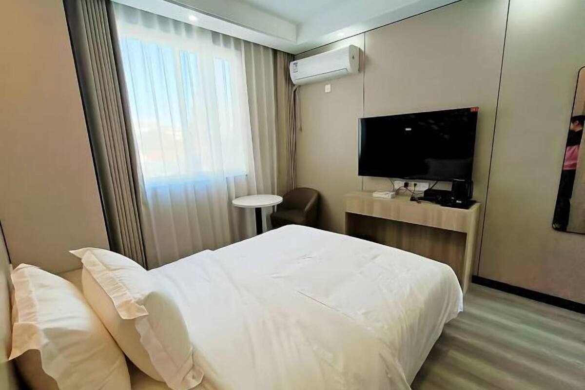 Ein Hotelzimmer mit einem Bett, einem Fernseher, einem kleinen Tisch und einer Klimaanlage.