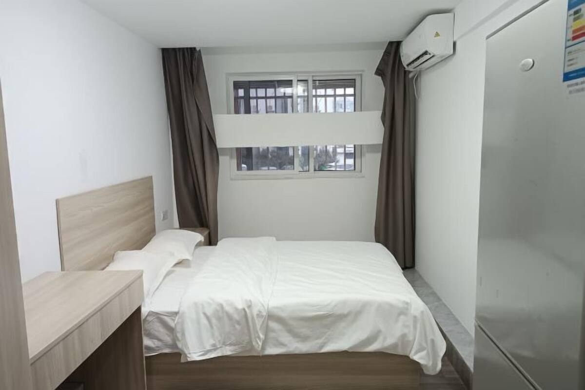 Ein kleines, sauberes Zimmer mit einem Etagenbett, einem Schreibtisch, einem Fenster mit Vorhängen und einer Klimaanlage.