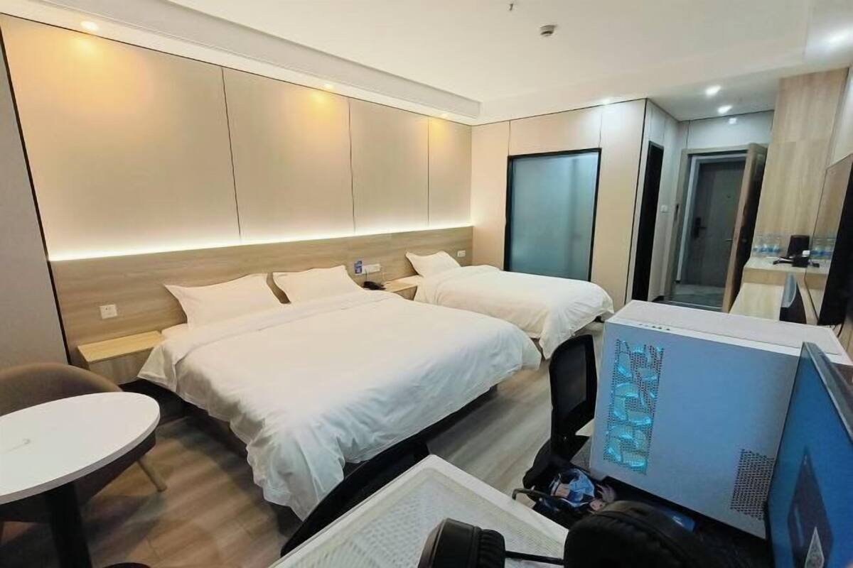 Ein Hotelzimmer mit zwei Betten, einem Schreibtisch, einem Stuhl, einem Computer und einem Spiegel.
