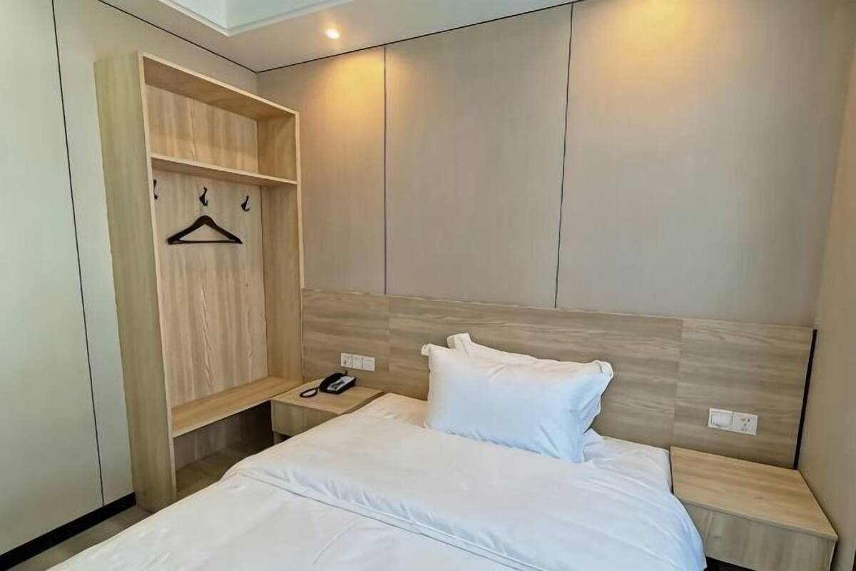 Ein Hotelzimmer mit einem Bett, einem Holzschrank, einem Nachttisch mit Telefon und einer Wandleuchte.