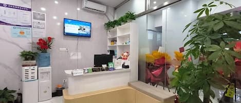 Un área de recepción con mostrador, televisor y plantas en macetas.