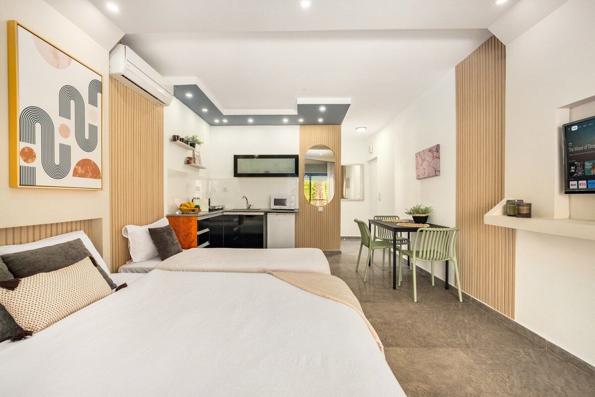 Ein modernes Hotelzimmer mit Bett, Schreibtisch, Stuhl und einer kleinen Küchenzeile.
