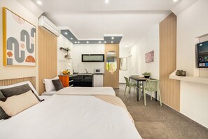Ein modernes Hotelzimmer mit Bett, Schreibtisch, Stuhl und einer kleinen Küchenzeile.