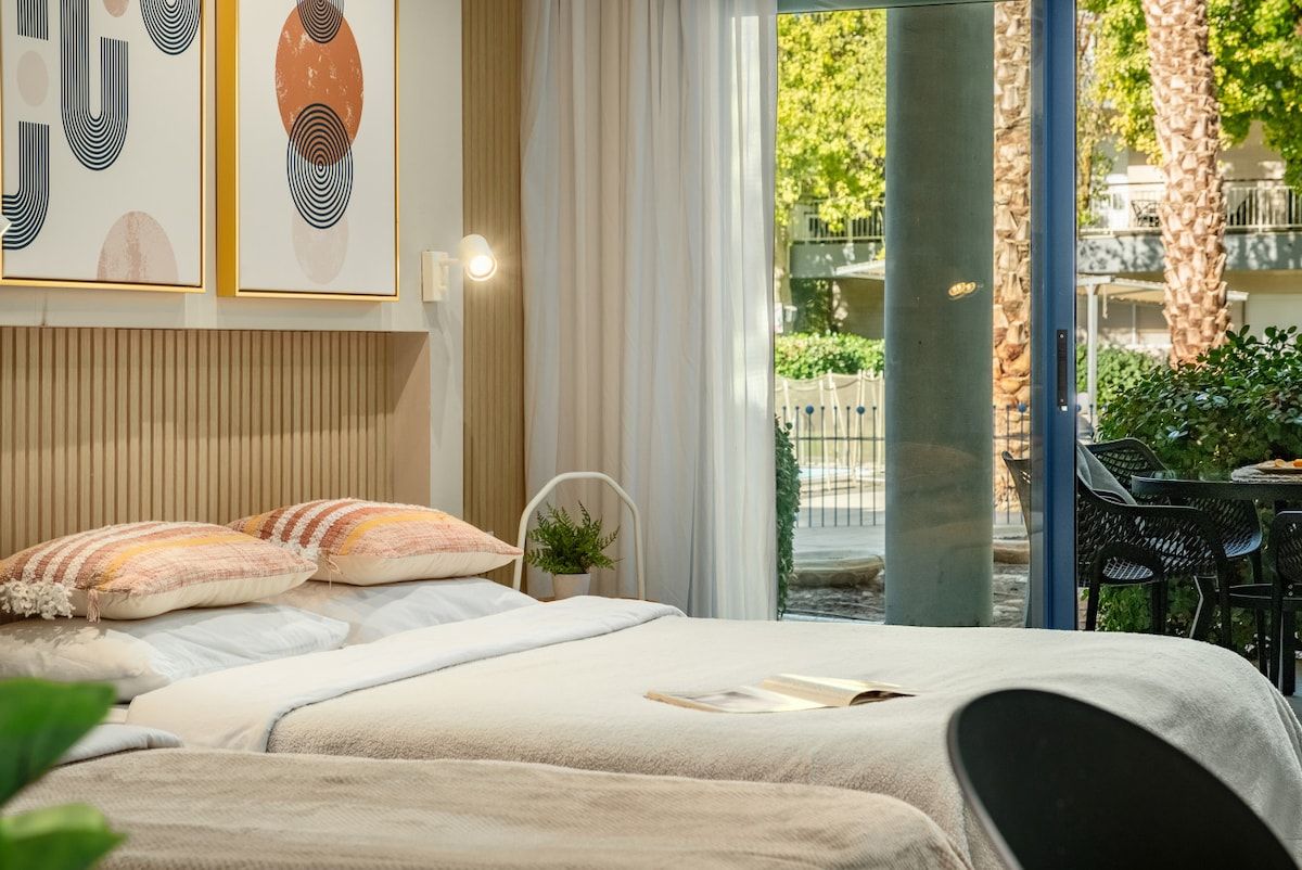 Ein Schlafzimmer mit einem Bett, Kissen, einem Nachttisch und einem Fenster mit Blick ins Freie.