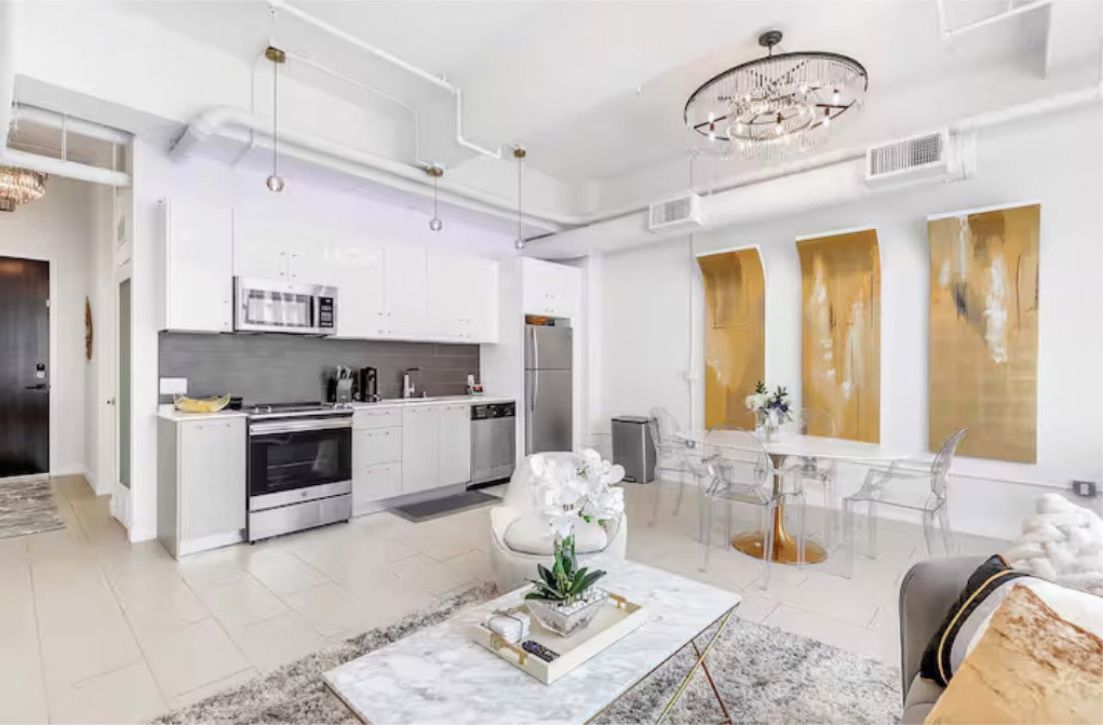 A modern kitchen with white cabinetry, stainless steel appliances, and a dining area with a marble table and clear chairs.