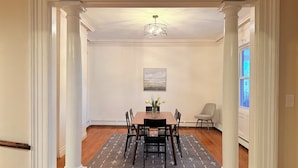 A dining area with a table, chairs, a vase with flowers, and a painting on the wall.