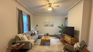 A living room with a sofa, armchairs, a coffee table, a TV, and a ceiling fan.
