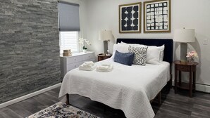 A bedroom with a stone accent wall, a bed with white bedding, two bedside tables with lamps, and artwork on the wall.
