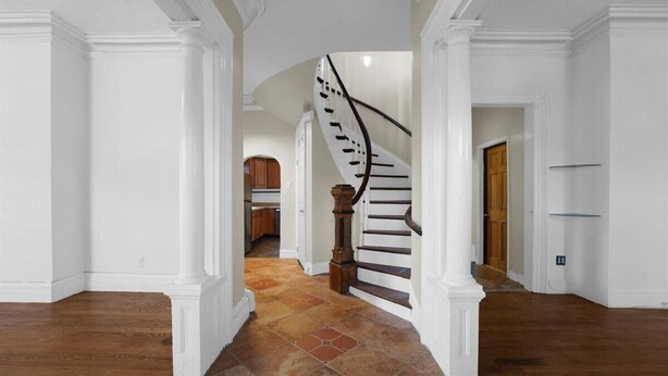 A spacious hallway with a wooden staircase leading to a kitchen area.