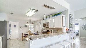 A modern kitchen with white cabinets, a central island with bar stools, a built-in microwave, and a stainless steel refrigerator. - Swim & Unwind: Pet-Friendly Home in Spring! (Spring)