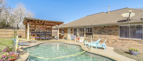 A backyard with a swimming pool, a covered patio, and a brick house.