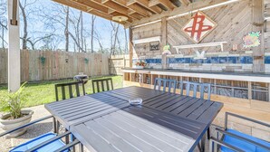 An outdoor patio with a wooden table and chairs, a barbecue grill, and a stone countertop with a decorative backsplash. - Swim & Unwind: Pet-Friendly Home in Spring! (Spring)