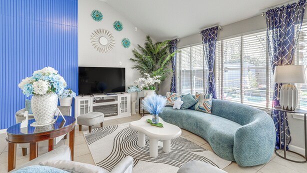A modern living room with a curved blue sofa, a flat-screen TV, a white cabinet, and decorative wall art. - Swim & Unwind: Pet-Friendly Home in Spring! (Spring)