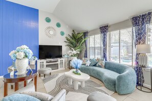 Un soggiorno moderno con un divano blu curvo, una TV a schermo piatto, un mobile bianco e decorazioni murali.