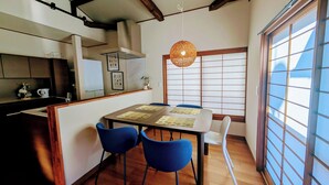 A modern kitchen with wooden beams, a dining area with blue chairs, and a large window with a view.